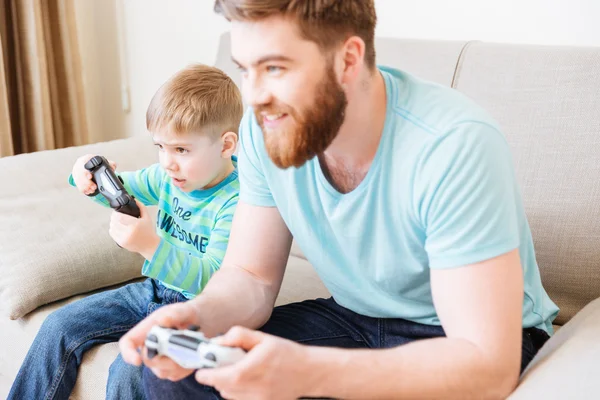 Мальчик играет в видеоигры с папой, сидящим на диване — стоковое фото