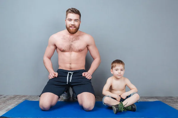 Happy dad and son sitting on blue yoga mat together