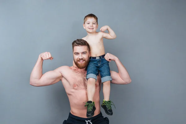 Cheerful man holding little son on shoulder and showing biceps — Stock Photo, Image