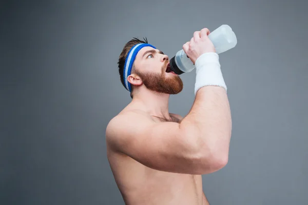 Shirtless bearded sportsman drinking water from plastic bottle — Stock Photo, Image