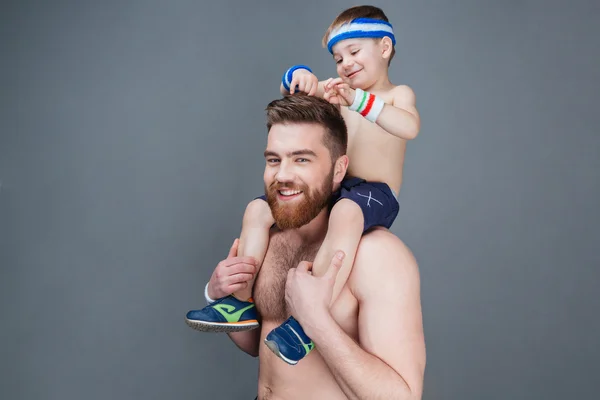 Niedlich lächelnder kleiner Junge sitzt auf den Schultern seines Vaters — Stockfoto