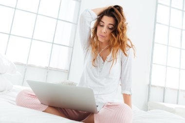 Laptop ve kulaklık ile yatağın üstüne oturan kadın