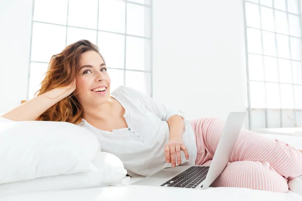 Frau im Schlafanzug liegt mit Laptop auf dem Bett — Stockfoto