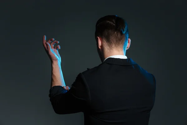 Vue arrière du jeune homme magicien debout avec la main levée — Photo