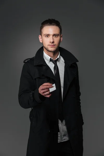 Confident businessman in black coat giving you blank business card — Stock Photo, Image