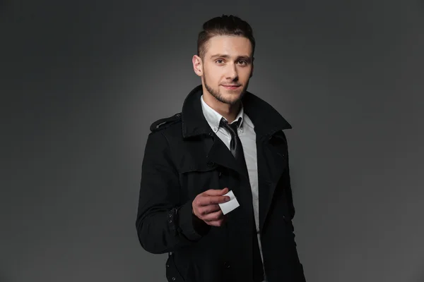 Businessman in black coat and tie giving blank business card — Stock Photo, Image