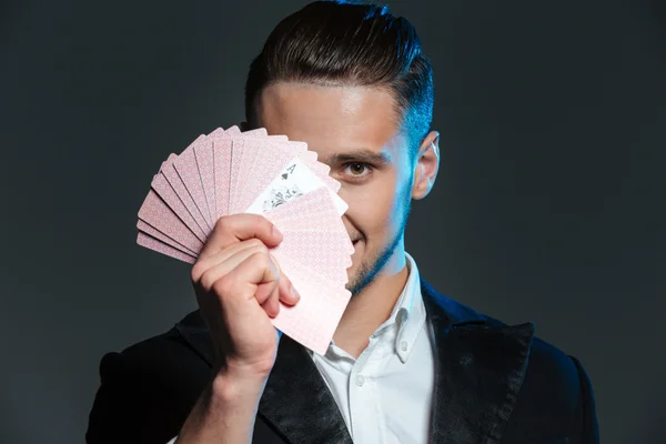 Leende ung man trollkarl täckt hans ansikte med spelkort — Stockfoto