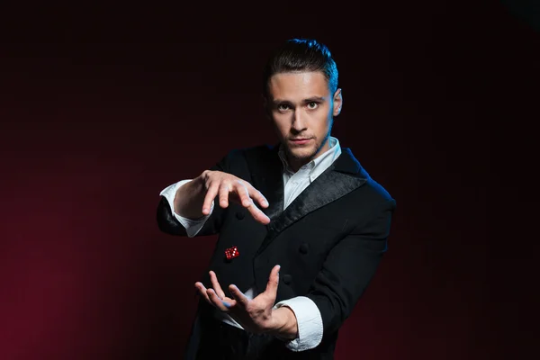 Confident young man magician showing tricks using one flying dice — Stock Photo, Image