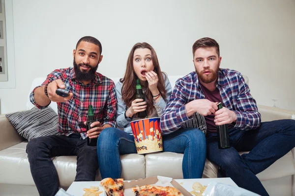 Zdumiony zszokowane przyjaciółki, oglądanie telewizji i jedzenie popcorn na kanapie — Zdjęcie stockowe