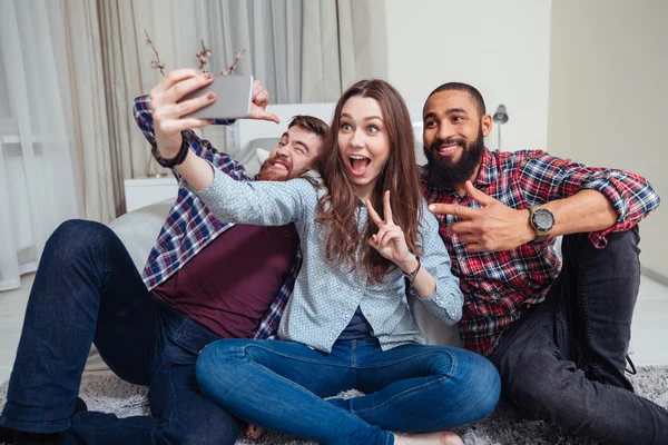 Szczęśliwy młodzi przyjaciele siedzi i biorąc selfie w domu — Zdjęcie stockowe