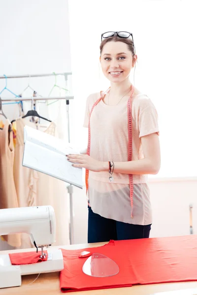 Donna felice sarta in piedi e lavorare con tessuto rosso — Foto Stock