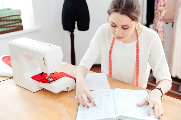 Serious woman seamstress thinking and reading notes in notebook — Stock Photo, Image