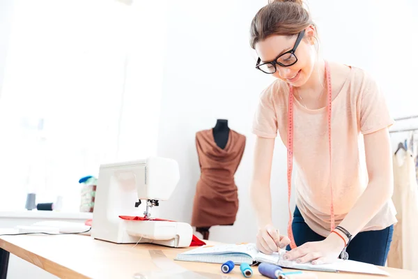 Mujer feliz costurera con gafas de pie y dibujo en el taller —  Fotos de Stock