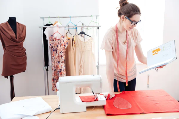 Femme sérieuse couturière travaillant avec du tissu rouge en studio — Photo