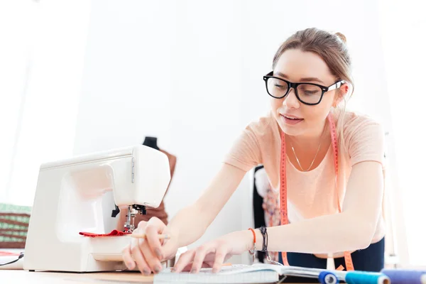 Donna cucitrice concentrata che indossa occhiali in piedi e lavora in officina — Foto Stock