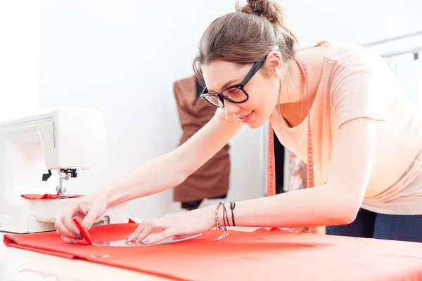 Focused woman tailor standing and drawing on red textile material — Stock Photo, Image