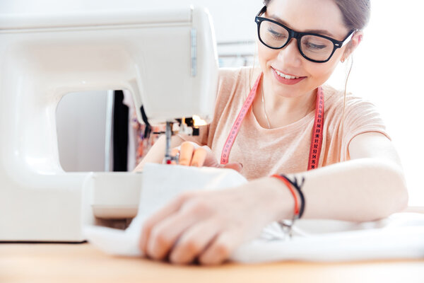 Улыбающаяся женщина шьет швейную машинку в мастерской
