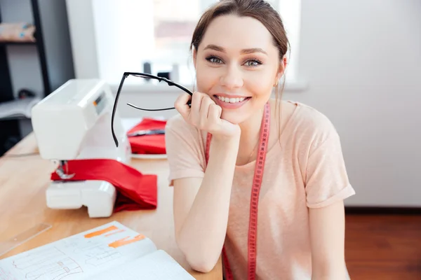 Mulher alegre costureira sentado e sorrindo no trabalho — Fotografia de Stock