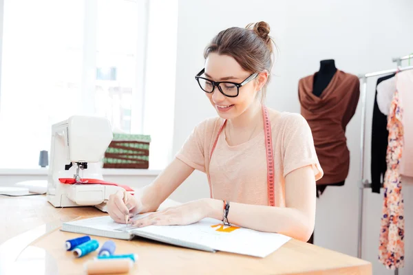 Femme souriante couturière dessin croquis et motifs à la table — Photo