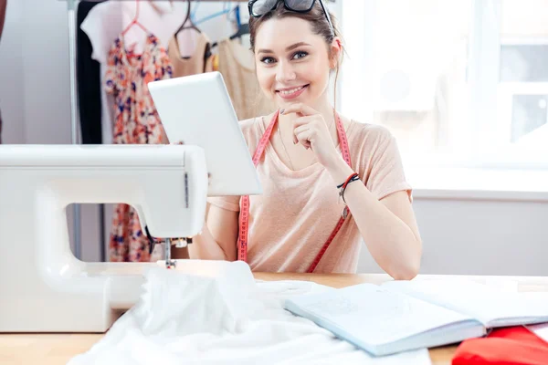 Cheerful woman seamstress smiling and using tablet at work — Stock Photo, Image