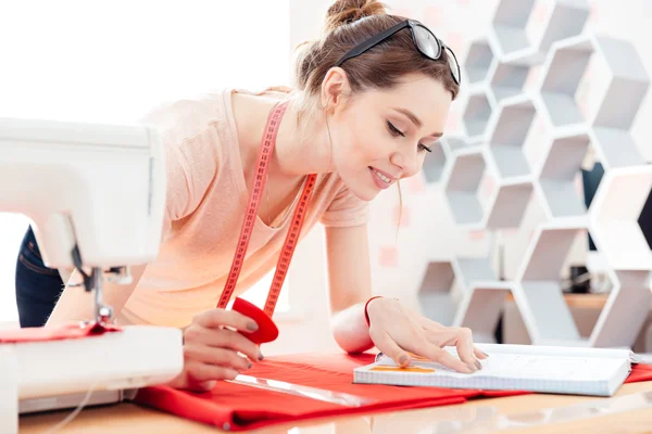 Mulher feliz costureira no trabalho com tecido vermelho — Fotografia de Stock