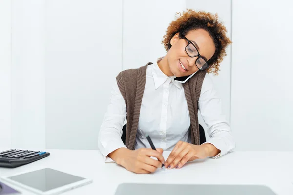 Contadora africana feliz hablando por teléfono celular y escribiendo — Foto de Stock