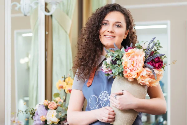 Mujer alegre florista sosteniendo florero con hermosas flores en la tienda — Foto de Stock