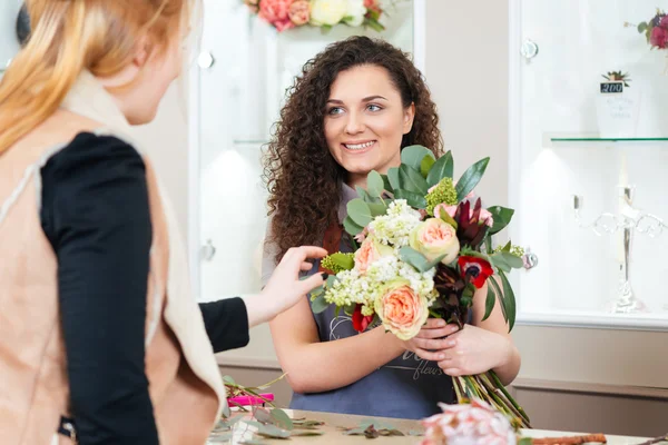 お客様に花の花束を示す笑みを浮かべて女性花屋 — ストック写真