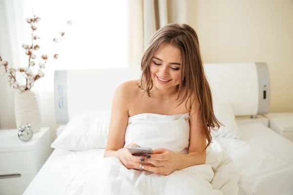 Mujer sentada en la cama y usando smartphone —  Fotos de Stock