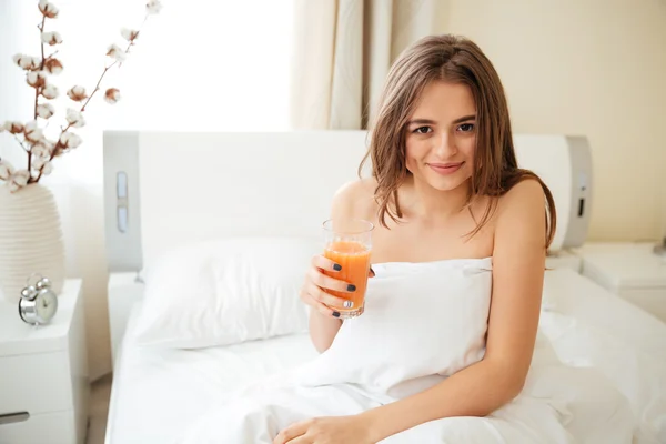 Mujer sentada en la cama y bebiendo jugo — Foto de Stock