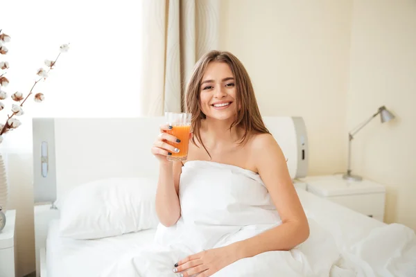 Усміхнена жінка тримає апельсиновий сік на ліжку — стокове фото