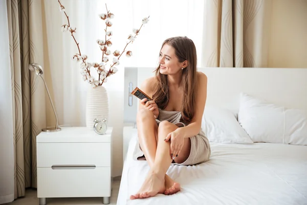 Femme appliquant de la crème sur les jambes et détournant les yeux — Photo