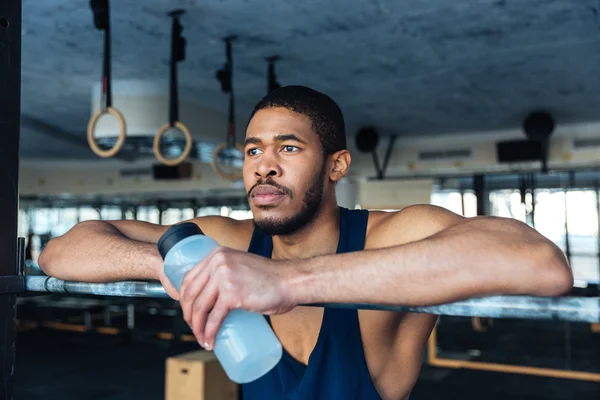 Pensive sports man holding bottle with water in the gym — Stock Photo, Image