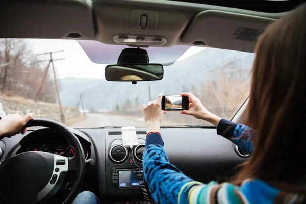 Pareja conduciendo en coche y tomando fotos con smartphone — Foto de Stock