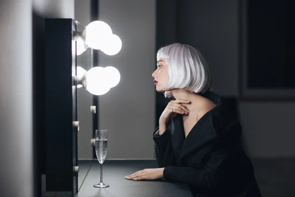 Mulher loira sentada e olhando para o espelho no vestiário — Fotografia de Stock