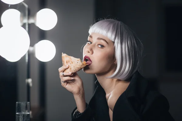 Δελεαστικό γυναίκα σε ξανθιά περούκα τρώγοντας πίτσα και πίνοντας σαμπάνια — Φωτογραφία Αρχείου