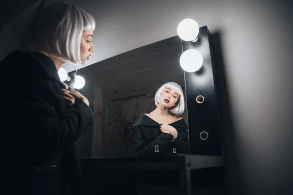 Woman in blonde wig sitting near mirror in dressing room — Stock Photo, Image