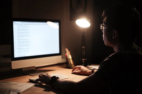 Homem concentrado usando computador sentado no quarto escuro em casa — Fotografia de Stock