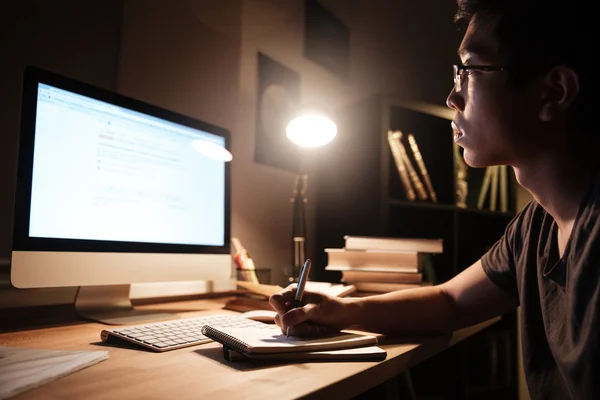 Homem focado witing e estudando usando o computador no quarto escuro — Fotografia de Stock