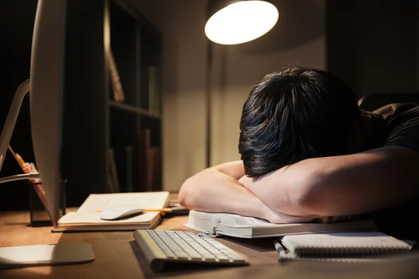 Homem exausto estudando e dormindo na mesa no quarto escuro — Fotografia de Stock