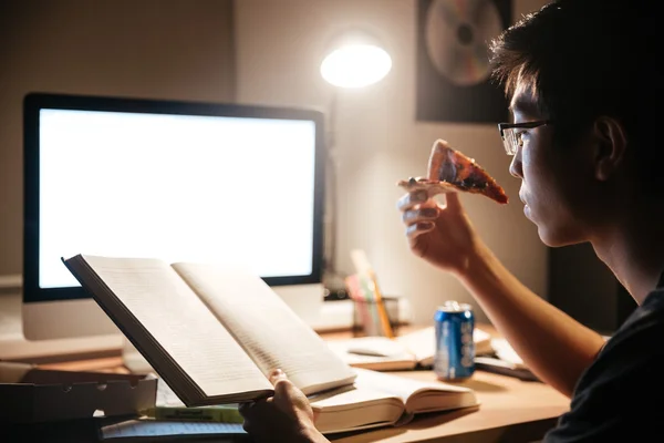 Focused man eating pizza and reading at nighttime — Stock Photo, Image