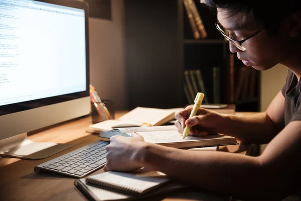 Seriöser Mann lernt mit Büchern und Computer im dunklen Raum — Stockfoto