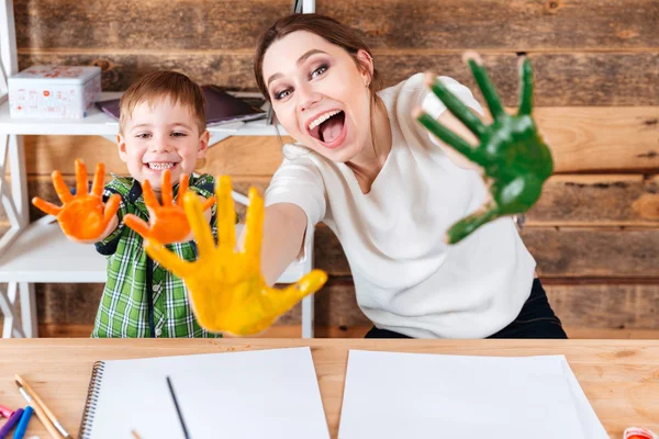 Mãe e filho felizes mostrando as mãos pintadas em tinta colorida — Fotografia de Stock