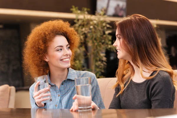 Två glada attraktiva unga kvinnor dricksvatten i café — Stockfoto