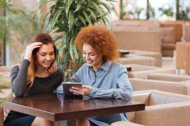Kafede oturan ve tablet birlikte kullanma iki gülümseyen kadın