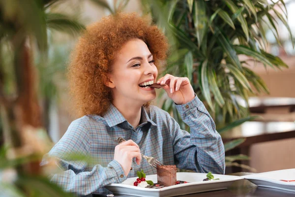 Feliz hermosa mujer sentada en la cafetería y comiendo postre de chocolate — Foto de Stock