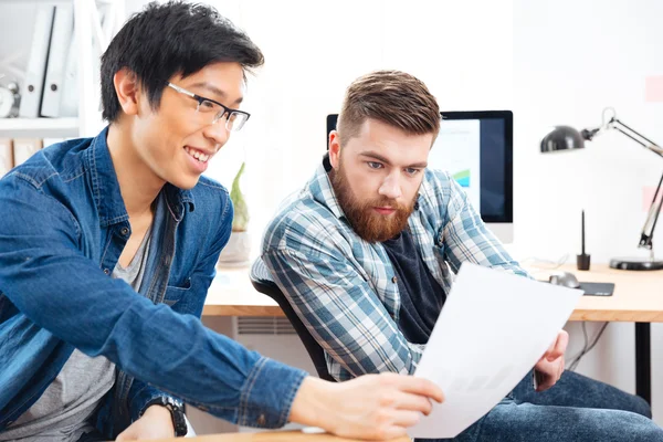 Two pensive men sitting and working with documents in office