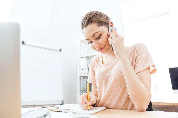 Donna sorridente che parla al cellulare e scrive in ufficio — Foto Stock