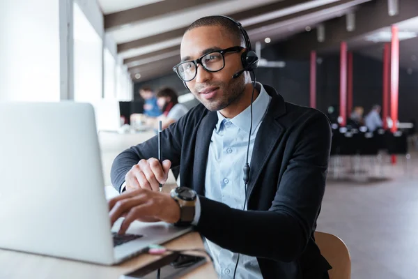 Uomo d'affari che lavora con il computer portatile utilizzando cuffie e microfono — Foto Stock