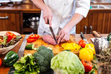 Professional chef cook cutting uncooked meat and fresh vegetables  clipart